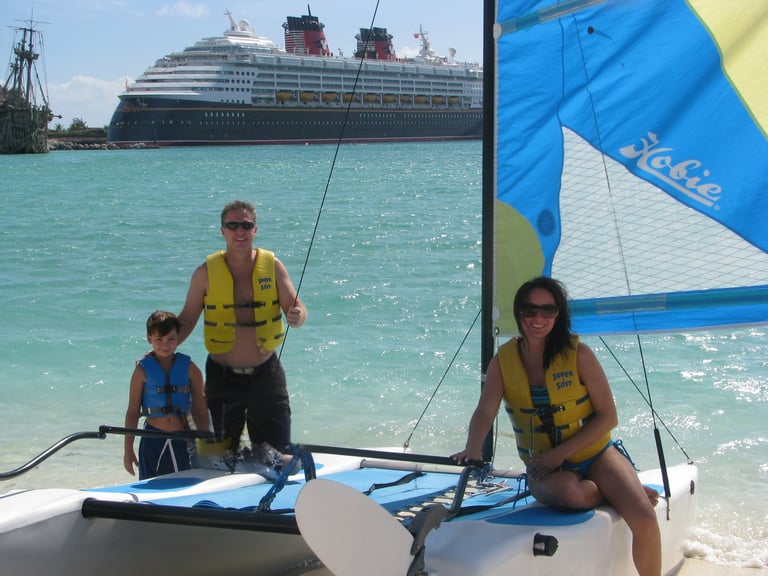 Family on sailboat in turquoise water with large cruise ship in background